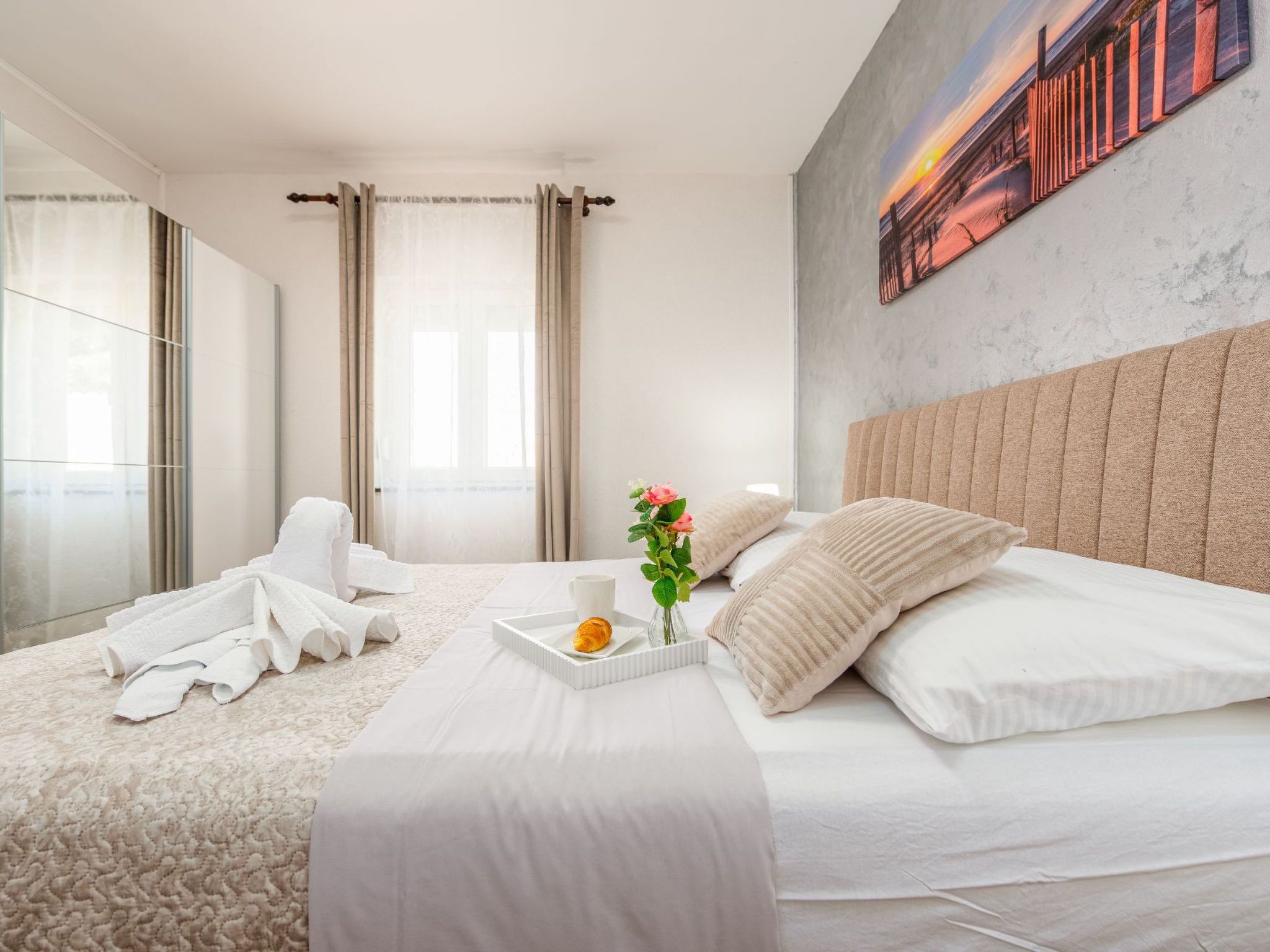 A modern hotel room with a large bed, a bedside table with a tray, and a painting on the wall.