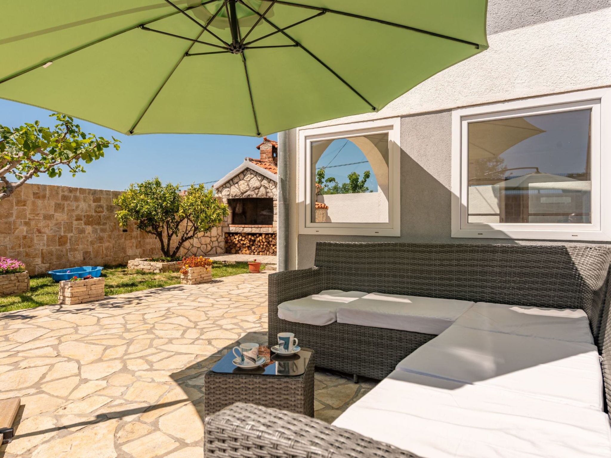 Un espace patio doté d’un sol en pierre, de sièges d’extérieur et d’un grand parasol.