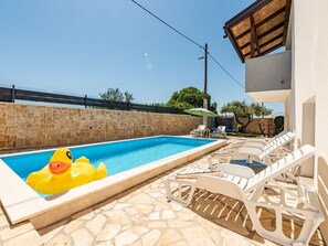 Ein Swimmingpool mit einer Schwimmenten, Steinmauern und Liegestühlen.