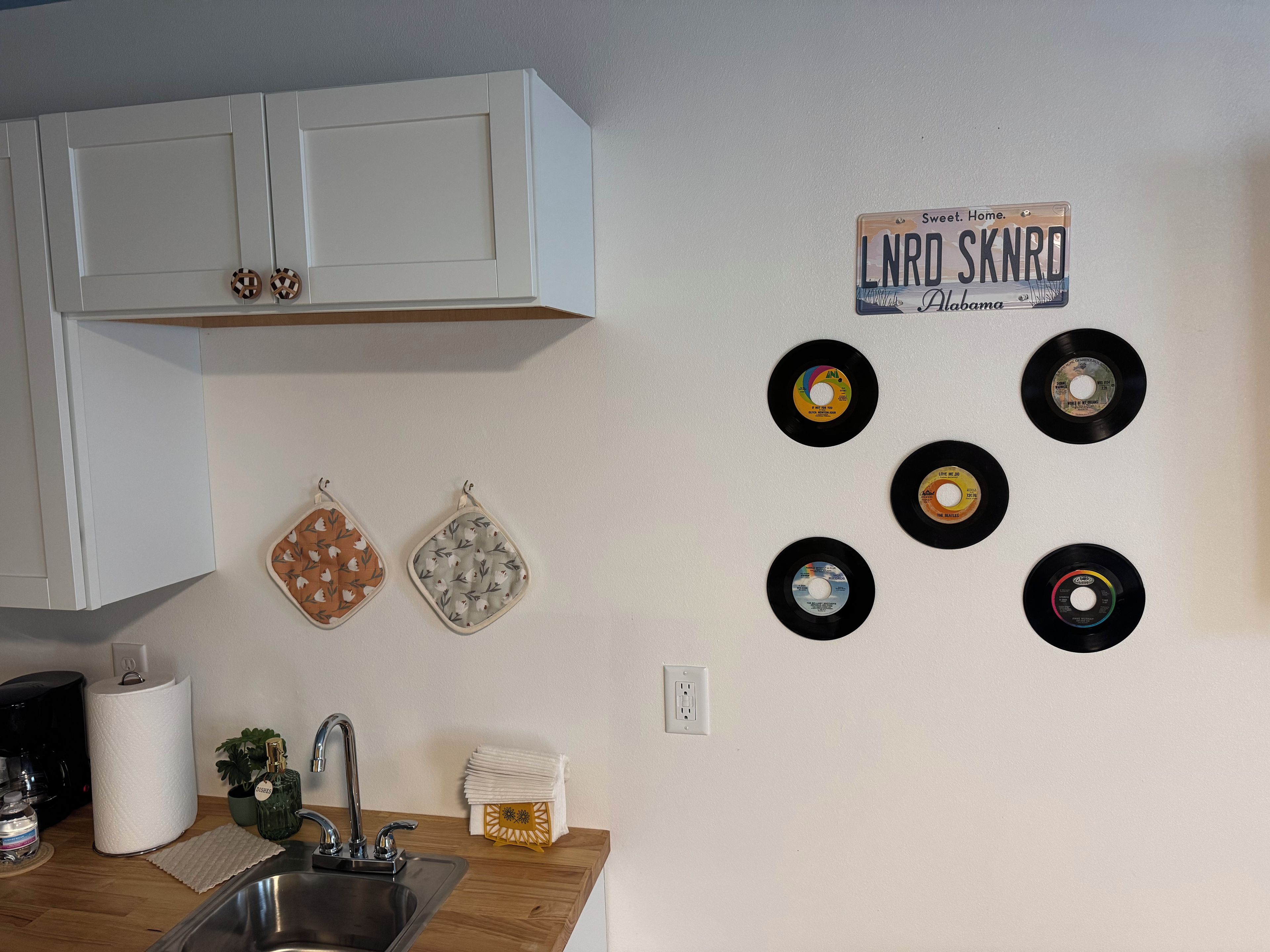 A kitchen with white cabinets, a sink, and a wall-mounted record player with six vinyl records.