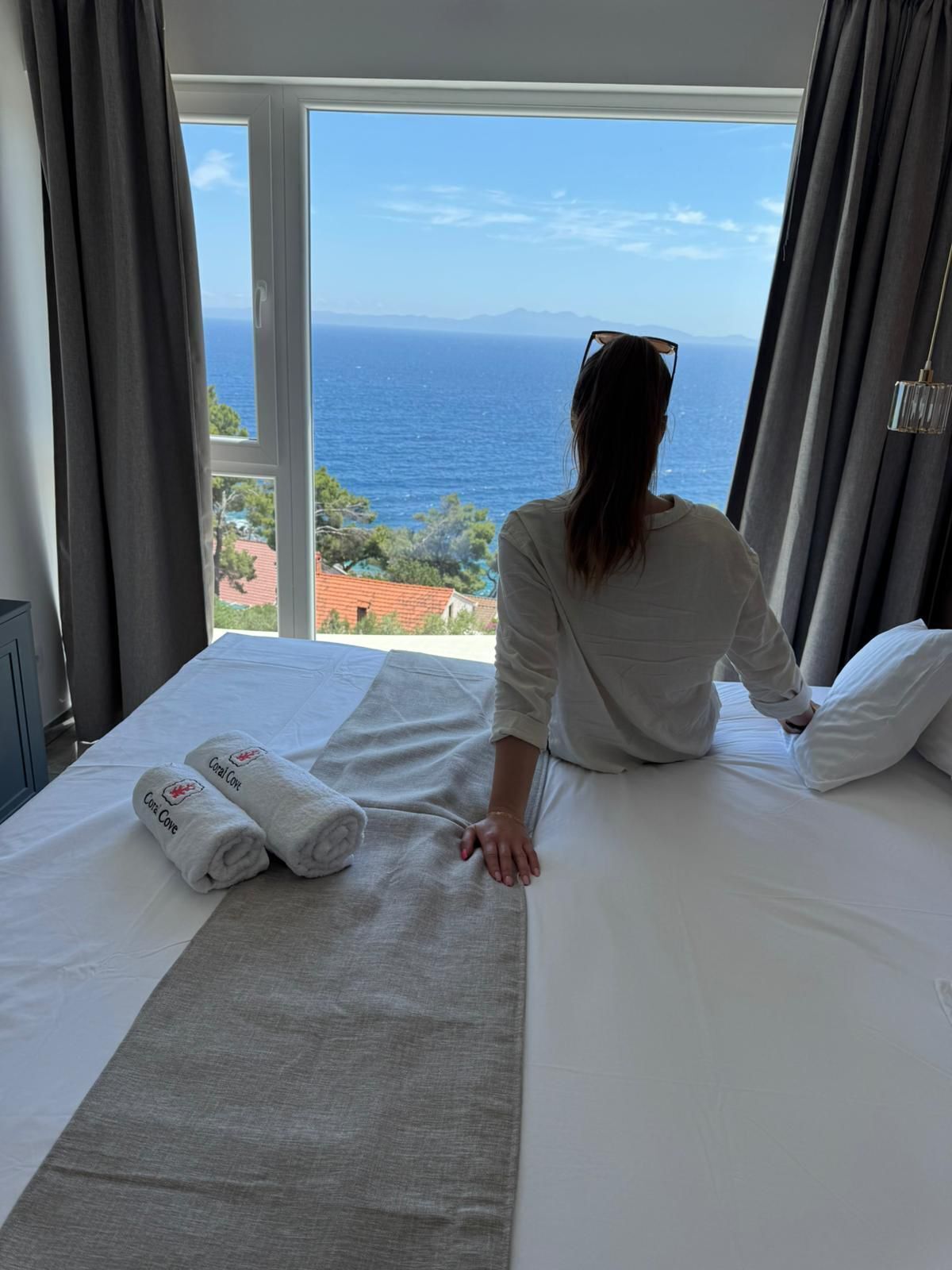 A hotel room with a bed, a view of the sea, and a window with curtains.