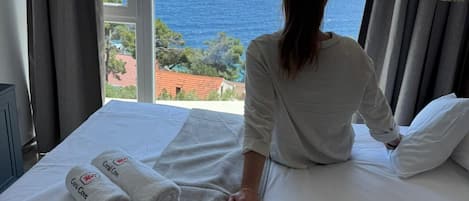 A hotel room with a bed, a view of the sea, and a window with curtains.