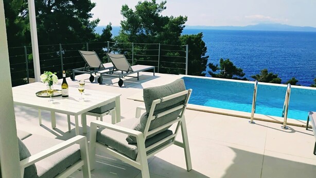 Ein Poolbereich mit Tisch, Stühlen und Blick auf das Meer.