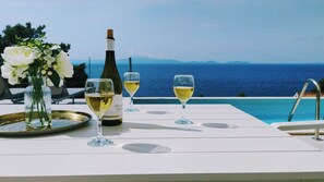 Une table avec une bouteille de vin, deux verres et un plateau, donnant sur une piscine et la mer.