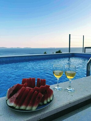 A poolside setting with a plate of watermelon slices and two glasses of white wine.