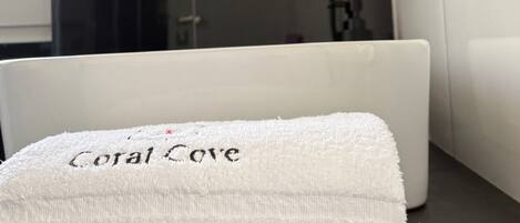 Un baño con una bañera blanca, una toalla con la etiqueta 'Coral Cove' y una zona de ducha.
