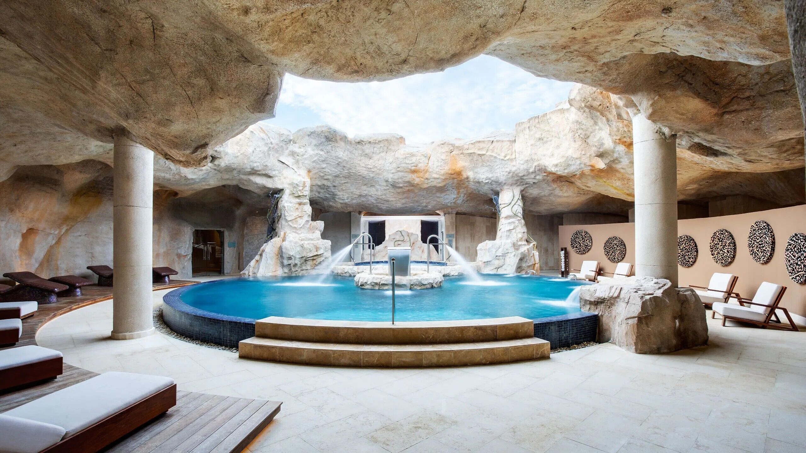 Un espace spa doté d’une piscine centrale, de coins salon et offrant une vue sur le ciel à travers des formations rocheuses.