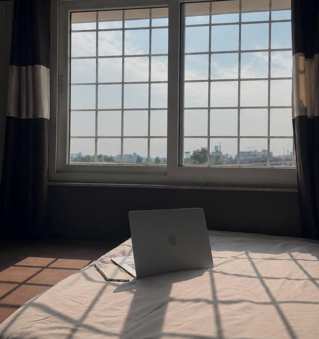 Une chambre avec un lit, un ordinateur portable et une fenêtre donnant sur un paysage urbain.