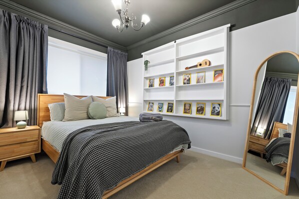 A bedroom with a bed, bedside tables, a mirror, a bookshelf, and a chandelier.