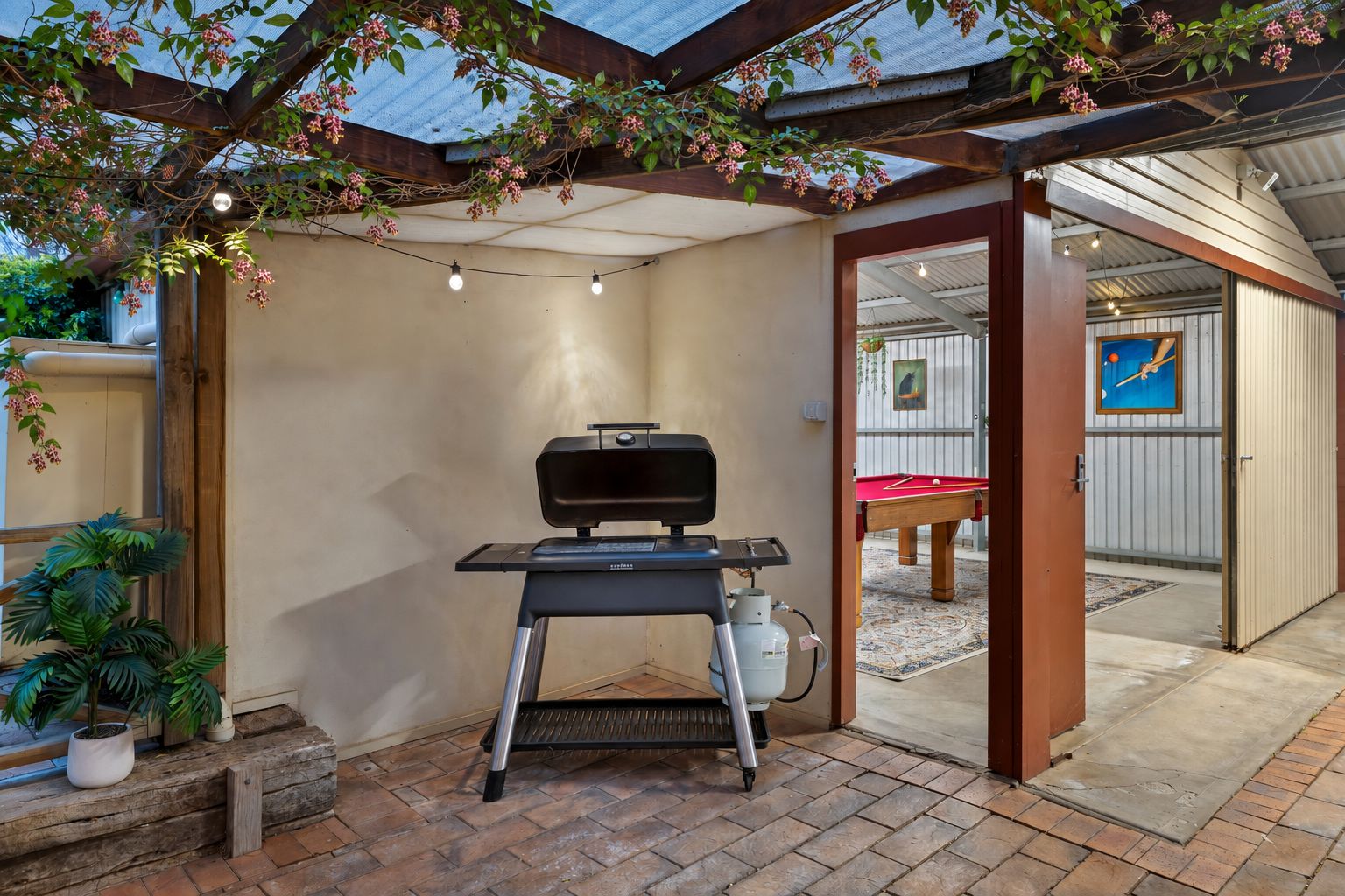 Un espacio exterior techado con una parrilla, plantas en macetas y una mesa de billar.