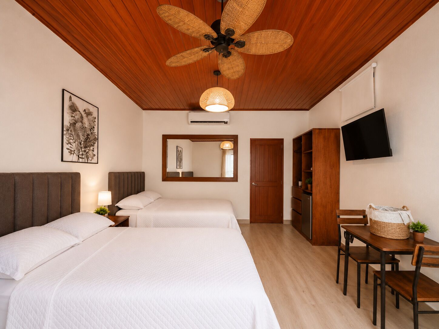 A hotel room with two beds, a ceiling fan, a TV, and a dining area with a table and chairs.