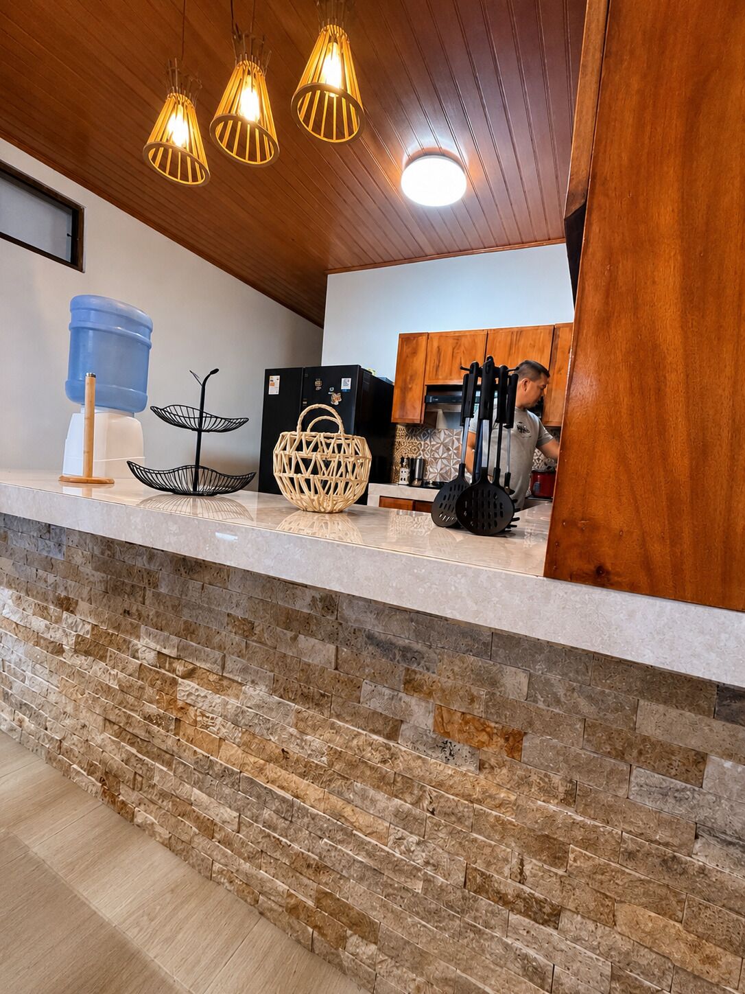 A kitchen with a stone countertop, wooden cabinets, and hanging pendant lights.