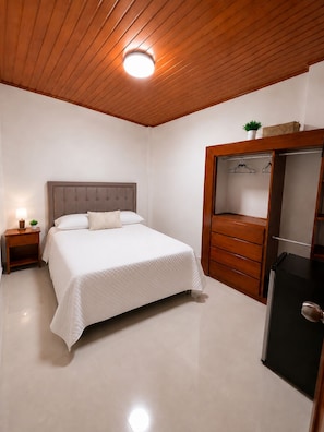 Een slaapkamer met een bed, nachtkastje, dressoir en spiegel.