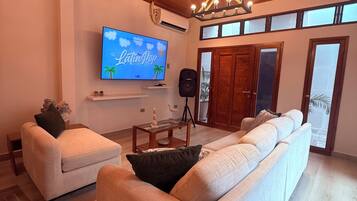 A living room with a large flat-screen TV, a wooden ceiling, and a modern chandelier.