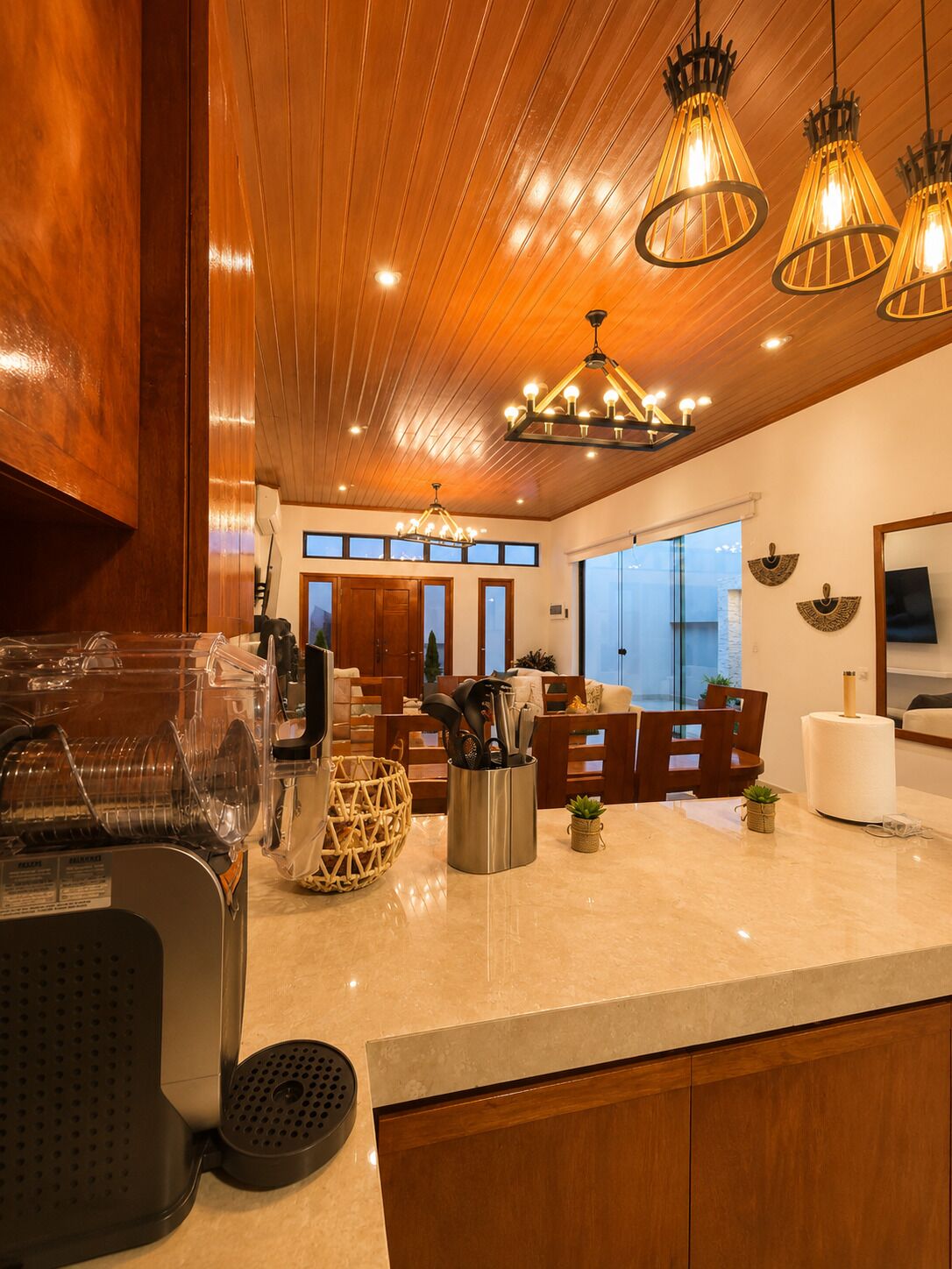 A modern kitchen with wooden cabinets, a marble countertop, and pendant lighting.