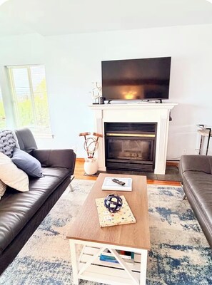 Ein Wohnzimmer mit Kamin, einem darüber montierten Fernseher, einer Couch, einem Couchtisch und einem Bücherregal.