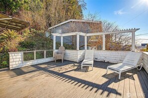 Um deck coberto ao ar livre com pérgola, duas poltronas de descanso e uma mesa pequena.