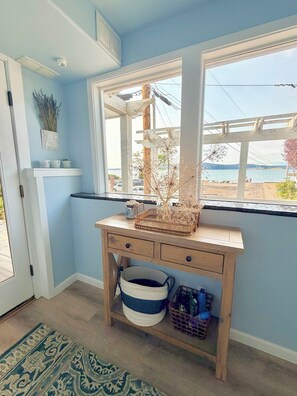 Une pièce avec un bureau en bois, une fenêtre donnant sur la mer, une porte et un tapis à motifs.