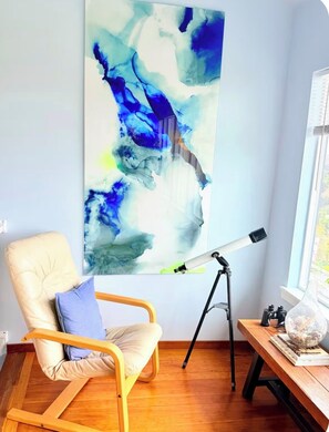 A room with a large abstract painting, a telescope, a wooden chair, and a wooden table with a bowl. - "The Launch” Beach Cottage on Camano Island (Camano)