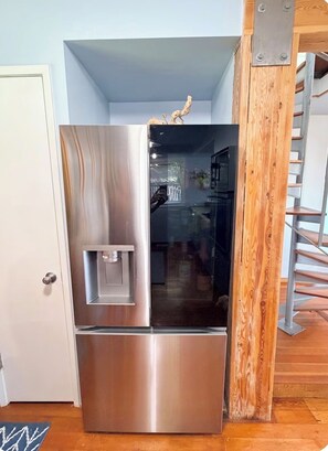A stainless steel refrigerator with a water dispenser, located in a kitchen with wooden accents and a visible staircase. - "The Launch” Beach Cottage on Camano Island (Camano)