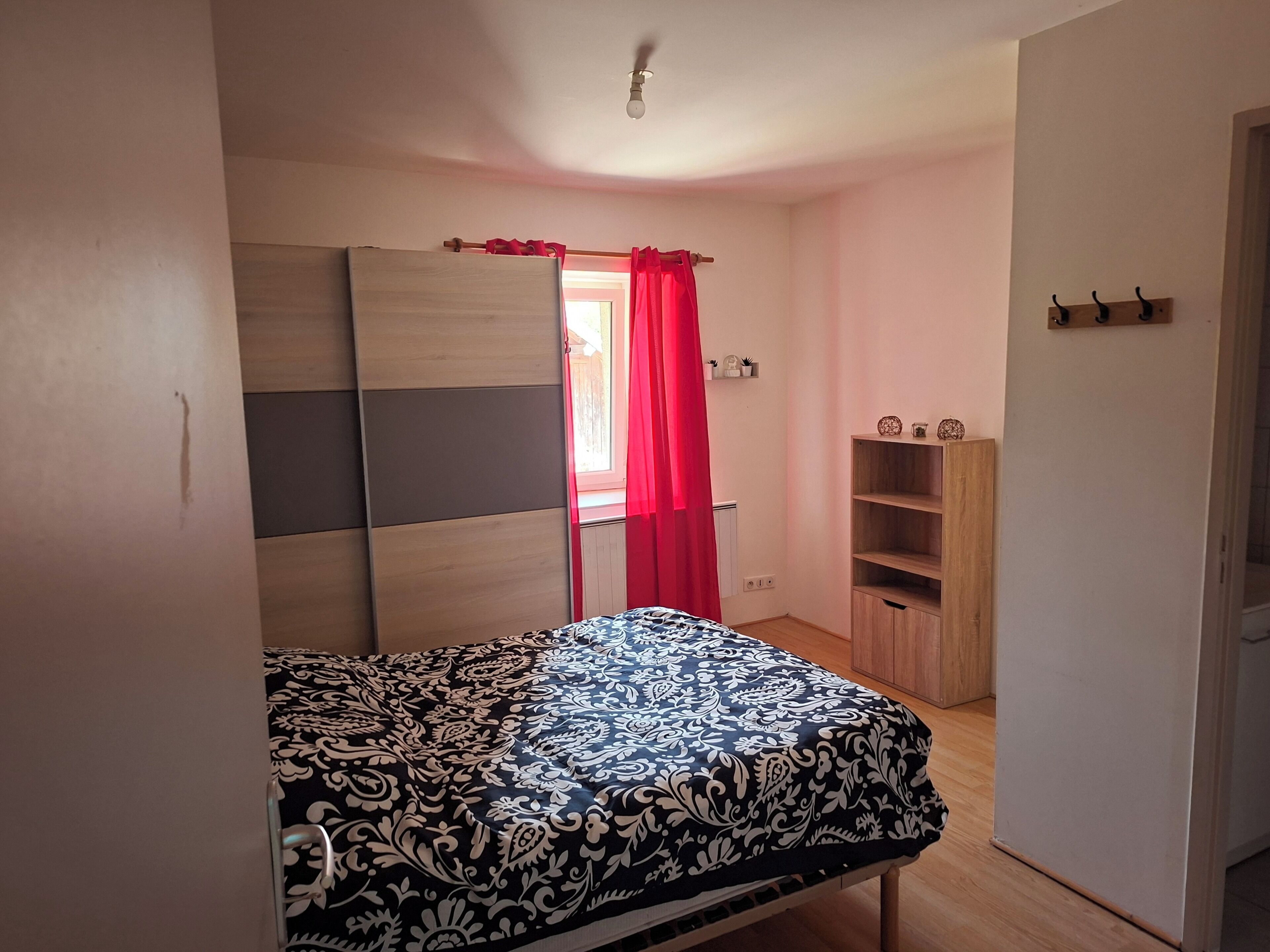 A bedroom with a bed, a wardrobe, a shelf unit, and a door with a red curtain.