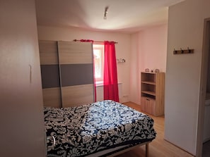 Une chambre à coucher avec un lit, une armoire, une étagère et une porte avec un rideau rouge.