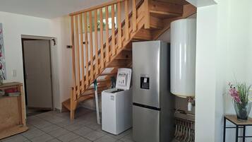 A kitchen with a wooden staircase, a refrigerator, a water dispenser, and a tiled floor.