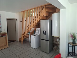 A kitchen with a wooden staircase, a refrigerator, a water dispenser, and a tiled floor.