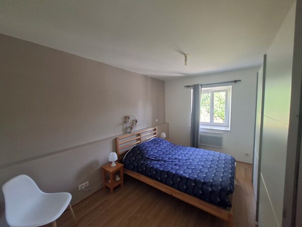 A bedroom with a bed, a chair, a bedside table, a window, and a ceiling fan.
