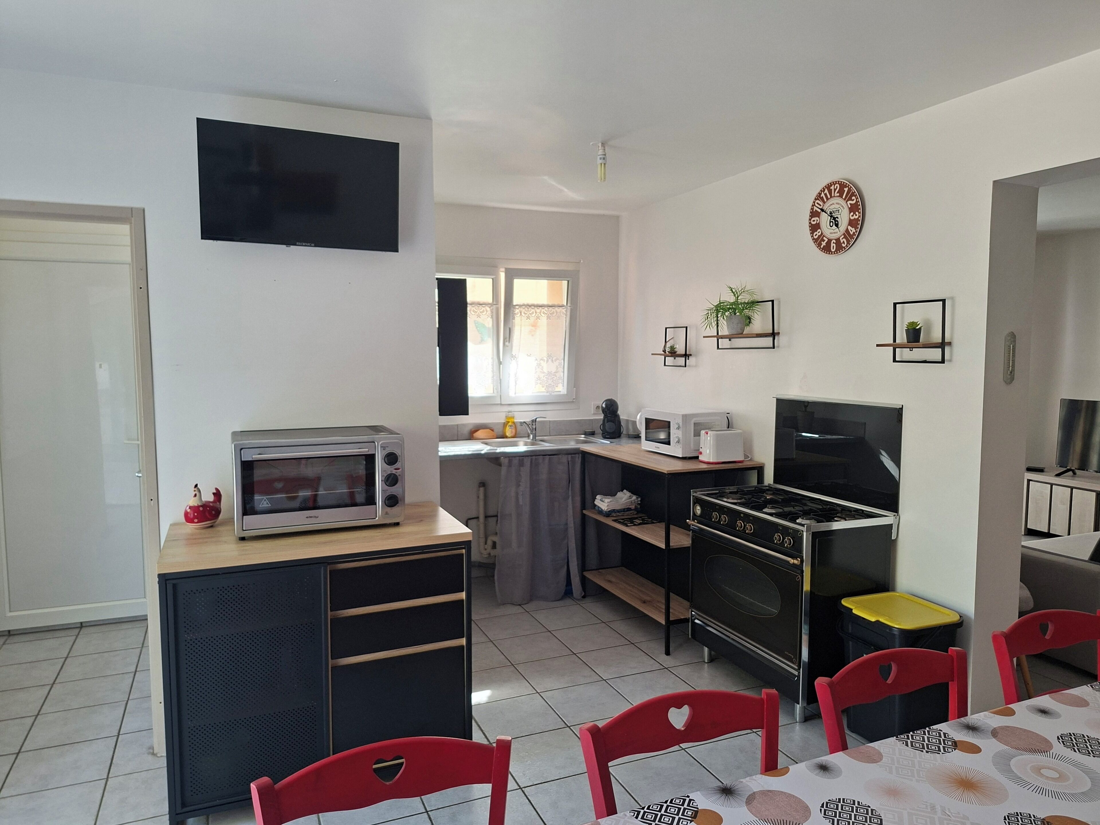 A compact kitchen with a microwave, toaster, and stove, a dining table with chairs, and a TV mounted on the wall.
