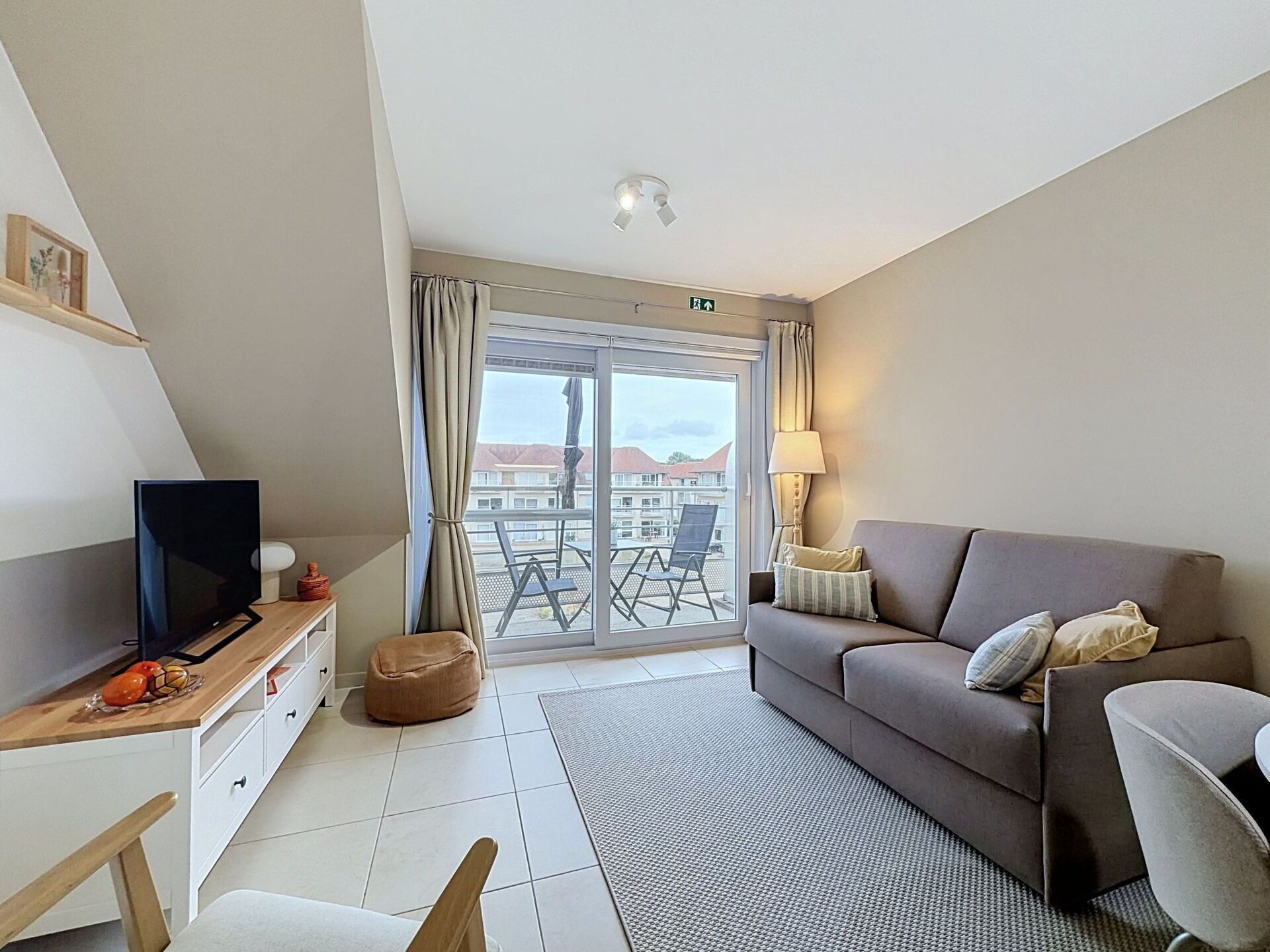 Un salon moderne avec un canapé, un téléviseur et un balcon aménagé avec du mobilier d’extérieur.