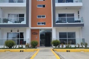 A multi-story hotel with a central entrance, balconies on each floor, and a parking area with yellow curbs. - Moderno, Seguro, Cerca Aeropuerto SDQ, Gym, 2 Parqueos (Santo Domingo Este)