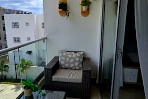 A balcony with a wicker sofa, a small table, and two potted plants. - Moderno, Seguro, Cerca Aeropuerto SDQ, Gym, 2 Parqueos (Santo Domingo Este)
