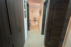 A hallway with dark wooden doors, a tiled floor, and a white wall with framed pictures. - Moderno, Seguro, Cerca Aeropuerto SDQ, Gym, 2 Parqueos (Santo Domingo Este)