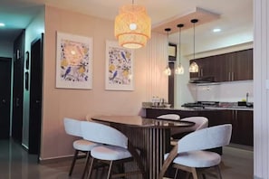 A modern kitchen with dark cabinets, a central island, pendant lighting, and two wall-mounted artworks.