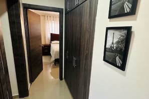 A hallway with a wardrobe, a bed with a white bedspread, and two framed pictures on the wall.