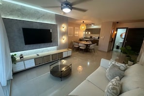 A modern living room with a flat-screen TV, a round coffee table, and a sofa with patterned cushions.