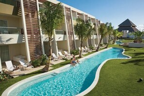 Une piscine entourée de chaises longues et de palmiers, le tout bordé d’un bâtiment doté de balcons.