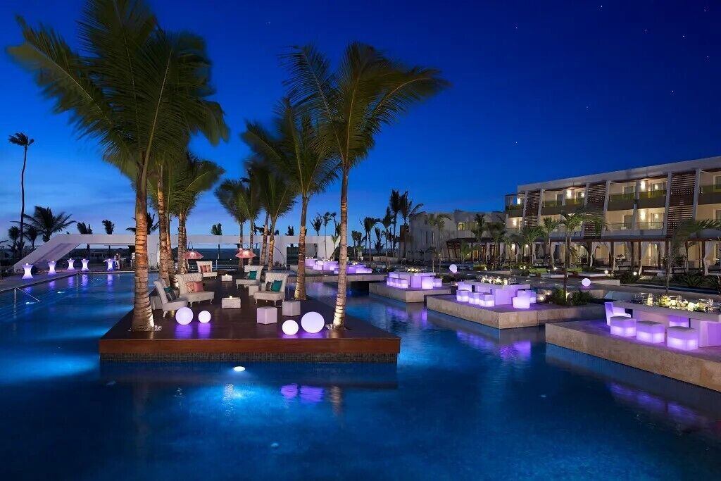 Ein Poolbereich mit Liegemöbeln und Palmen, umgeben von einem Gebäude mit mehreren Balkonen.