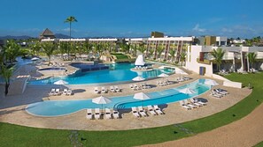 Un resort con varias piscinas, tumbonas y palmeras.