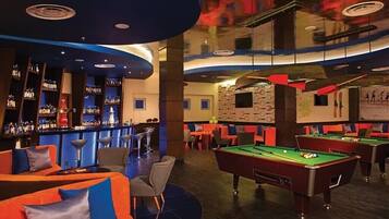 Un área de bar con mesas de billar y asientos, una barra con botellas de licor y un mural en la pared.