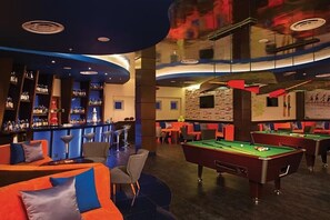 Un área de bar con mesas de billar y asientos, una barra con botellas de licor y un mural en la pared.