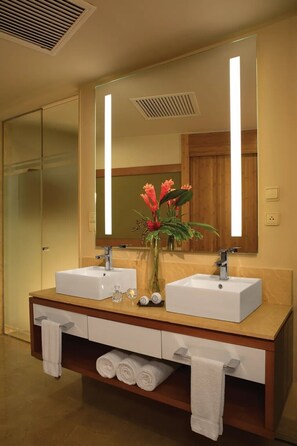 Une salle de bain avec deux lavabos, un grand miroir et un vase rempli de fleurs.