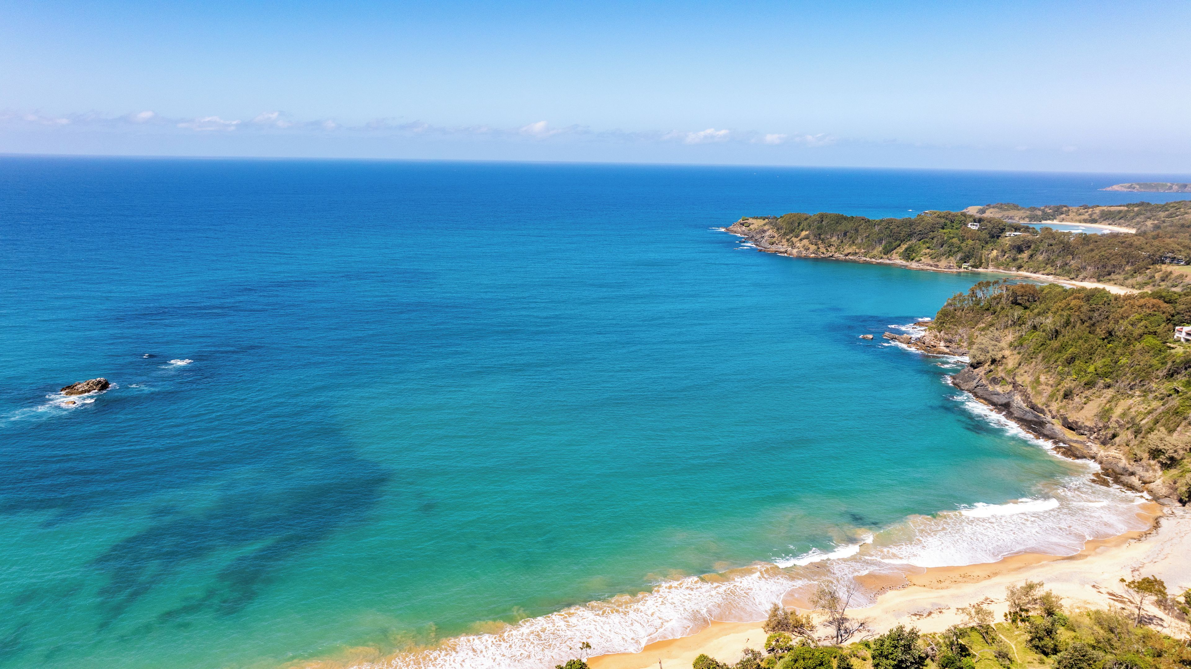 A coastal landscape with a beach, clear blue sea, and a hilly terrain.