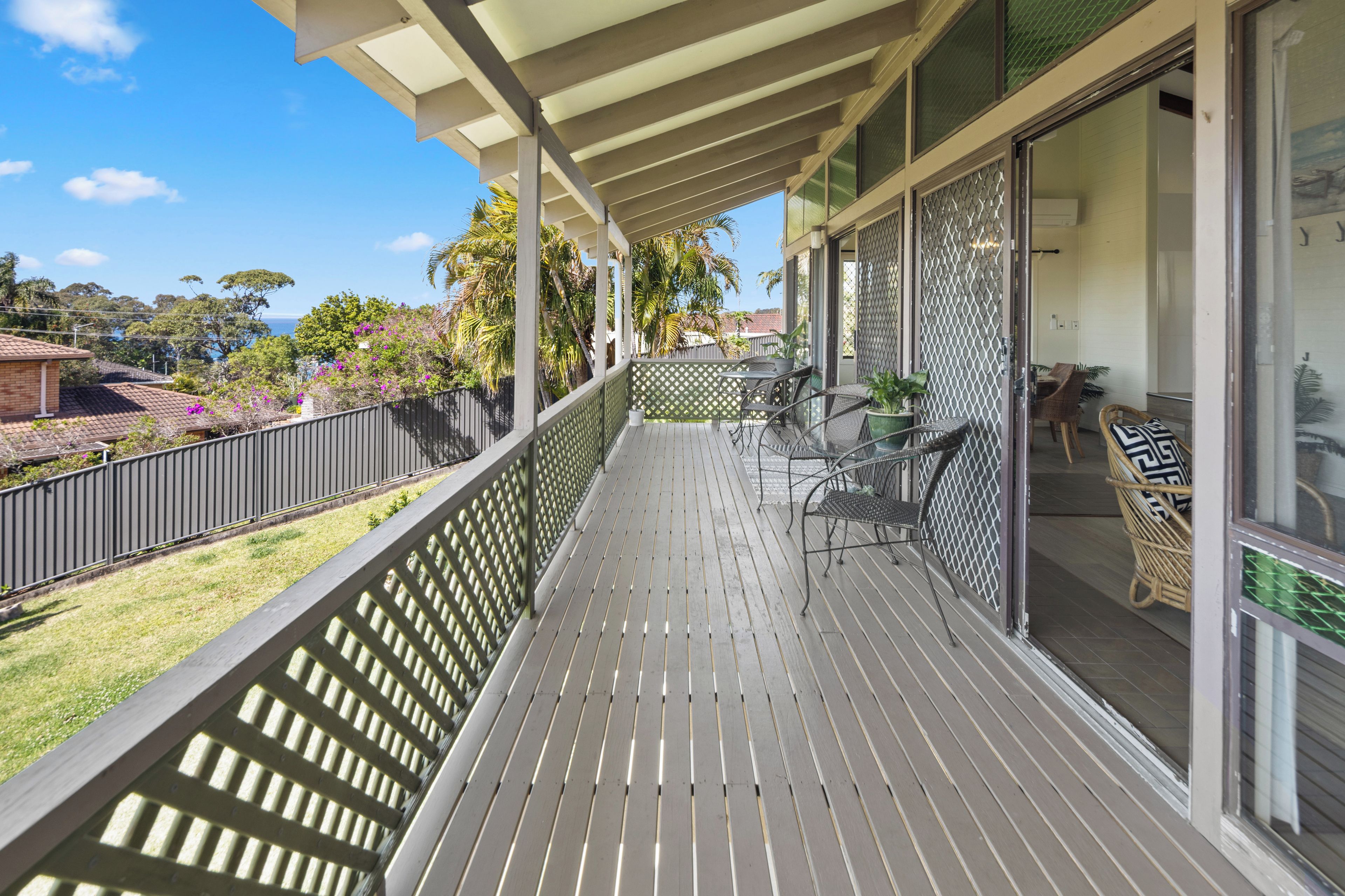 A wooden deck with outdoor furniture, a view of the sea, and a fenced garden area.
