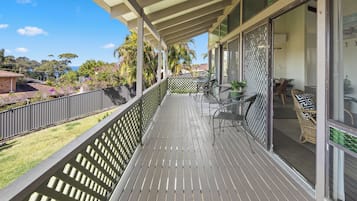 A wooden deck with outdoor furniture, a view of the sea, and a fenced garden area.