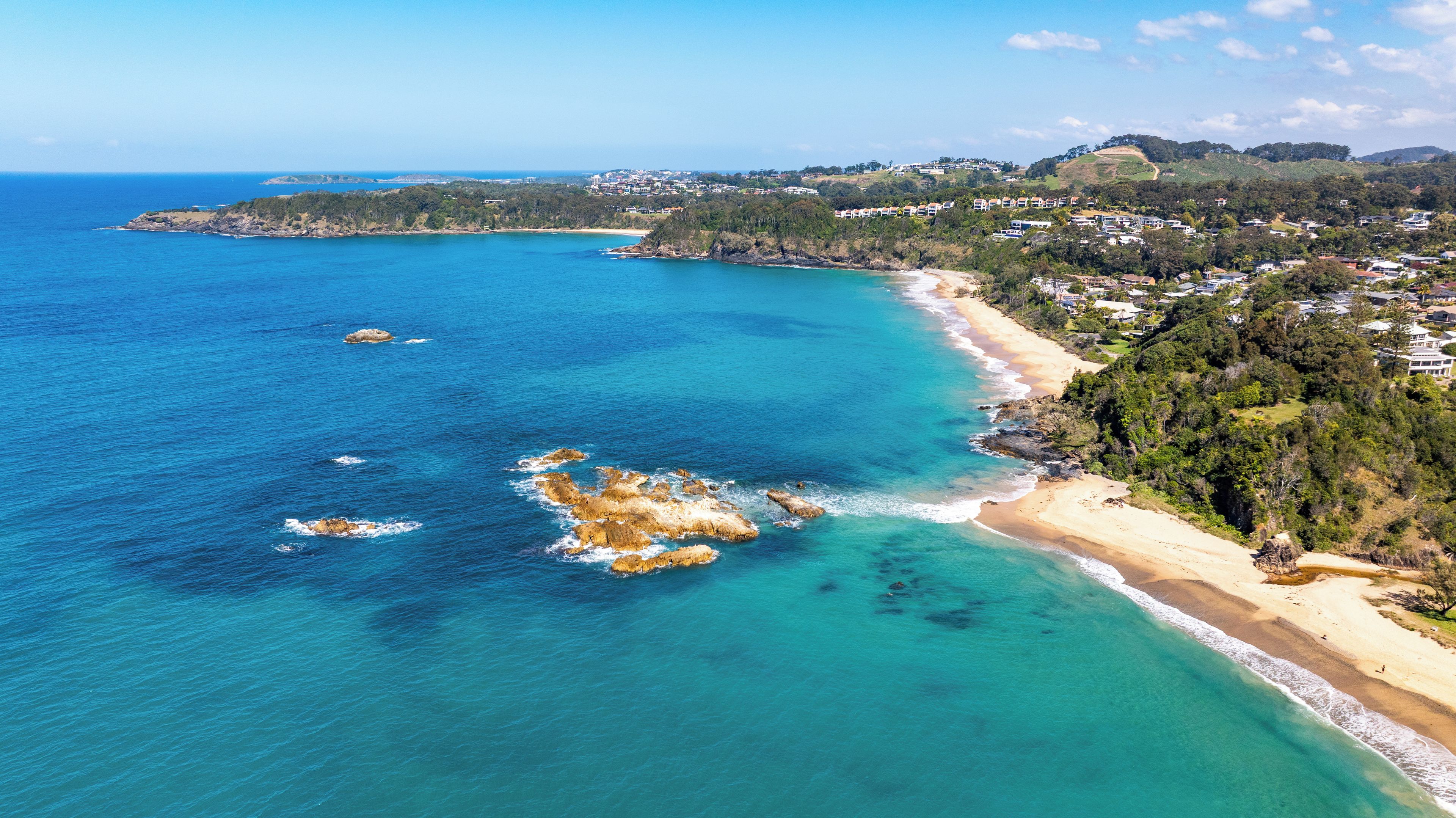 Eine Küstenlandschaft mit Strand, klarem blauen Wasser und hügeliger Landschaft im Hintergrund.