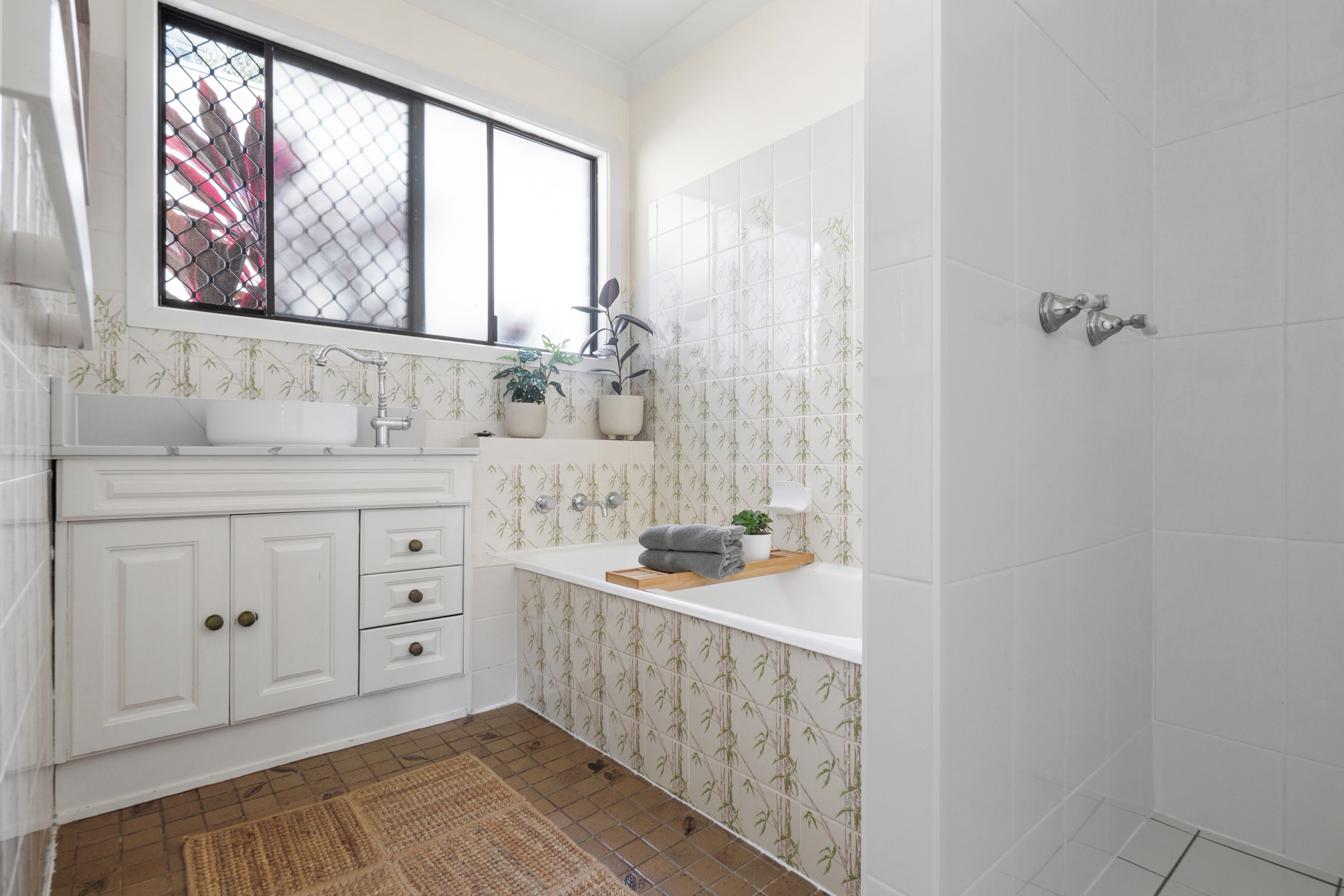 A bathroom with a white sink, a window, a shower, and a patterned wall.