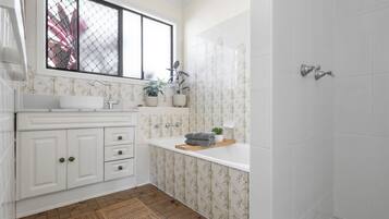 A bathroom with a white sink, a window, a shower, and a patterned wall.