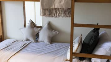 A bunk bed with a headboard, two pillows, a blanket, and a hanging macrame piece.